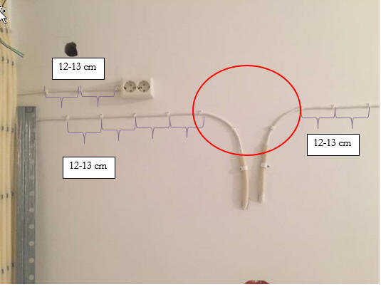 Elektriska kablar fästa på vägg med klämmor markerade för att visa 12-13 cm avstånd, med en markerad vinkel.