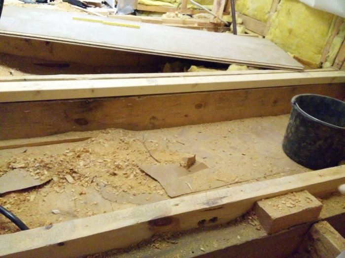 Puulattian rakentaminen työmaalla, sahajauhoja ja musta ämpäri näkyvissä. Taustalla lastulevyä odottamassa asennusta.