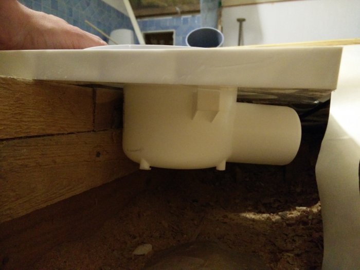 Kuva näyttää valkoisen viemäriputken päätyvän taustan puupaneelien viereen, mahdollisesti asennettuna altaan tai vessanpöntön alle.