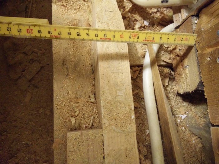 Mitt kuvaa puulattiarakenteita, joissa mittanauha näyttää noin 20 cm etäisyyttä. Oikealla valkoisia putkia ja puulastuja ympärillä.