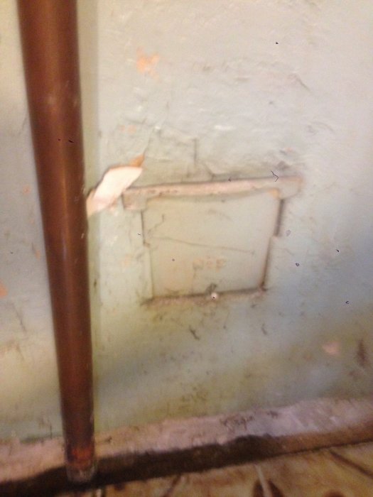 Gammal dold renslucka vid murstock och en kopparledning i ett renoveringsprojekt av ett källarbadrum.