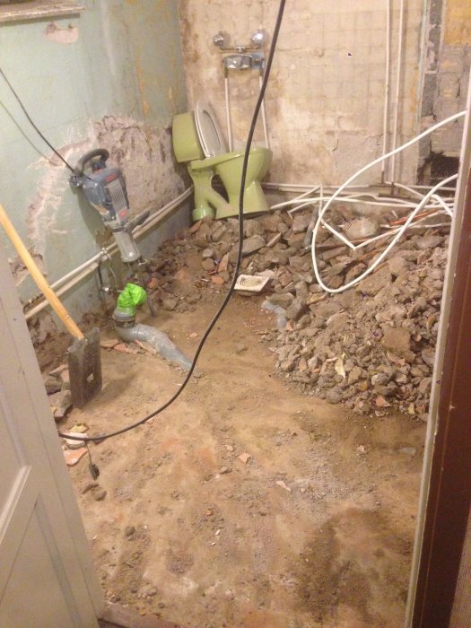 Rivningsarbete i en källare med högar av skräp, synliga rör och gammal toalett.