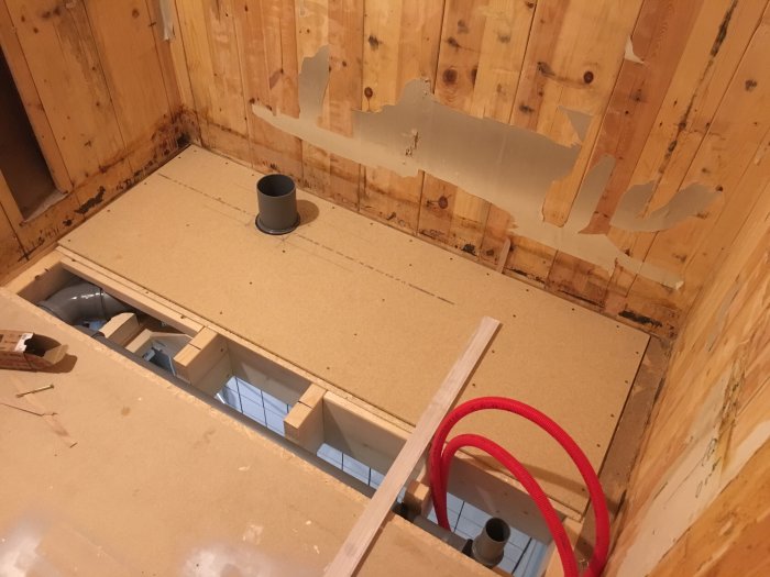 Ett pågående badrumsrenoveringsprojekt med nyinstallerat 22mm golvspån och synliga vattenrör och avlopp.