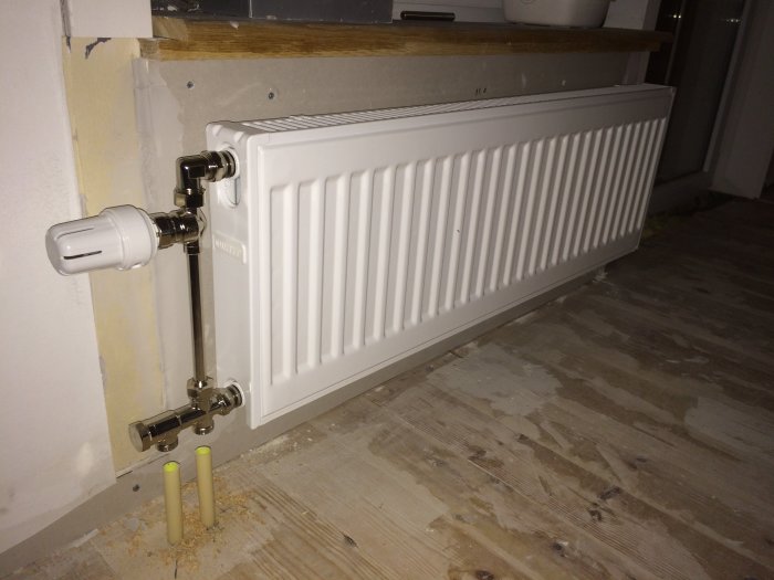 Nyinstallerad vit radiator med anslutningar för ett 2-rörssystem på en renoverad vägg.