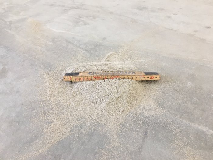 Slipdamm samlad i en hög på en betongyta med ett måttstock placerat ovanpå för skala.