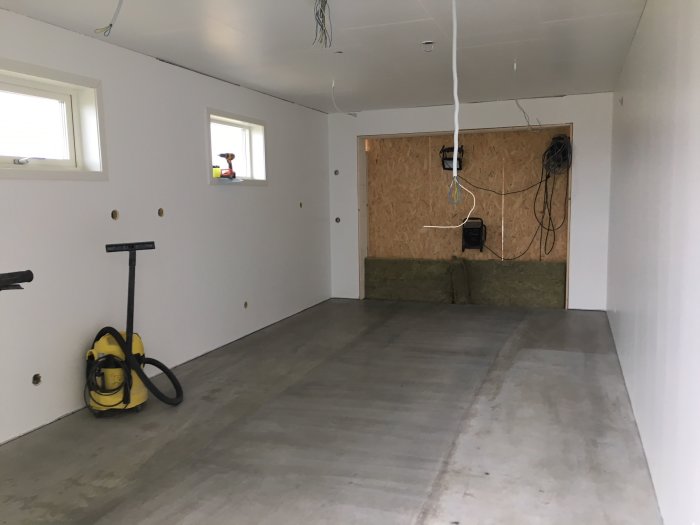 Betonggolv efter slipning med ABS-slipmaskin och gult dammsugare i ett oinrett rum med oslipat blyertsstreck.