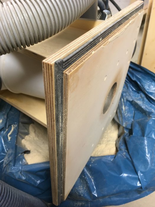 Fernissad björkplywood med överfalsat lock och e-profillist nära en fräs med dammsamlare.