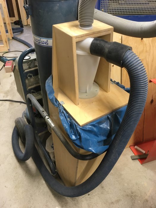 Träcyklon för dammutsug med fernissad björkplywood och anslutna sugslangar i en verkstad.