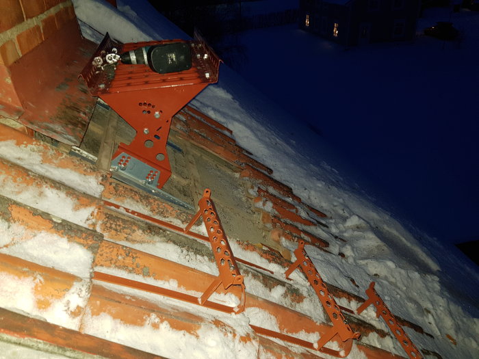 Rödlackerade stag och bryggfästen installerade på ett snötäckt tak i skymningen.