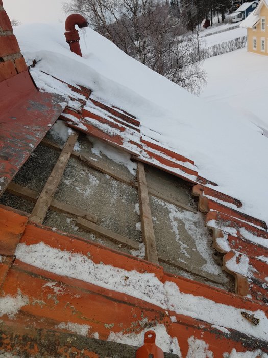 Rödlackerade stag och bryggfästen monterade på ett snötäckt tak med tegelpannor.