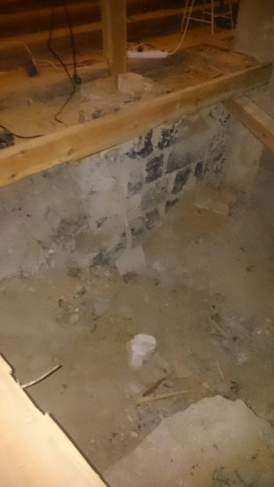 En spade som står upp i ett mörkt, ostädat byggrum med betonggolv och slumpmässigt byggmaterial.