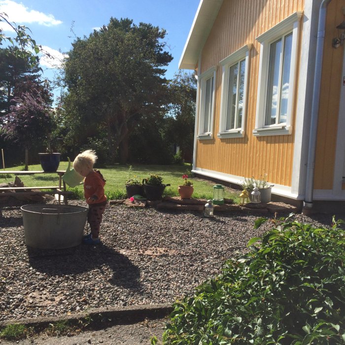 Ettåring står i gruset framför gult hus med pågående renovering av övervåningen, soligt väder.