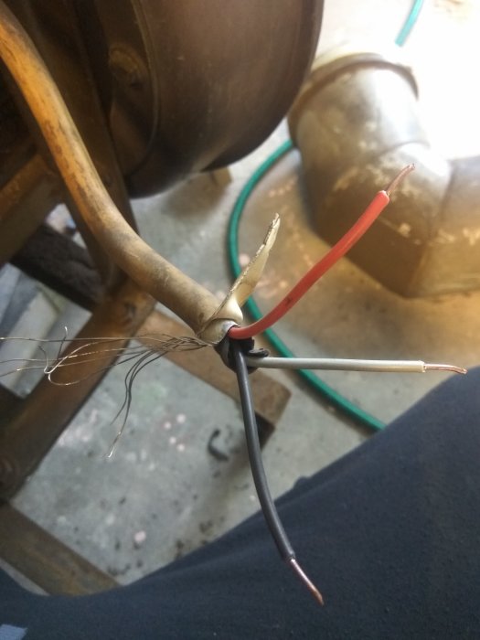 Ändar av tre elektriska kablar, en röd, en svart och en vit, är frilagda och förtvinade i en verkstadsmiljö.