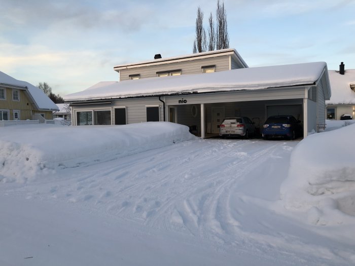 Ett hus med carport och bilar i vintersnö.