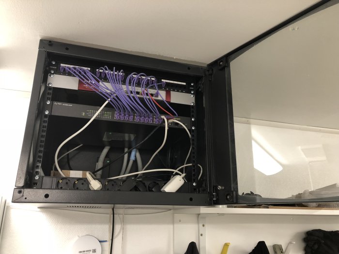 Ett öppet nätverksskåp med patchpanel, ethernet-switch och sladdar monterat på en vägg.