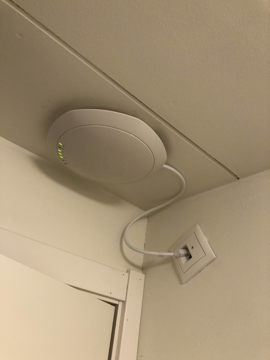 Trådlös router monterad på vägg med synlig Ethernet-kabel och vägguttag.