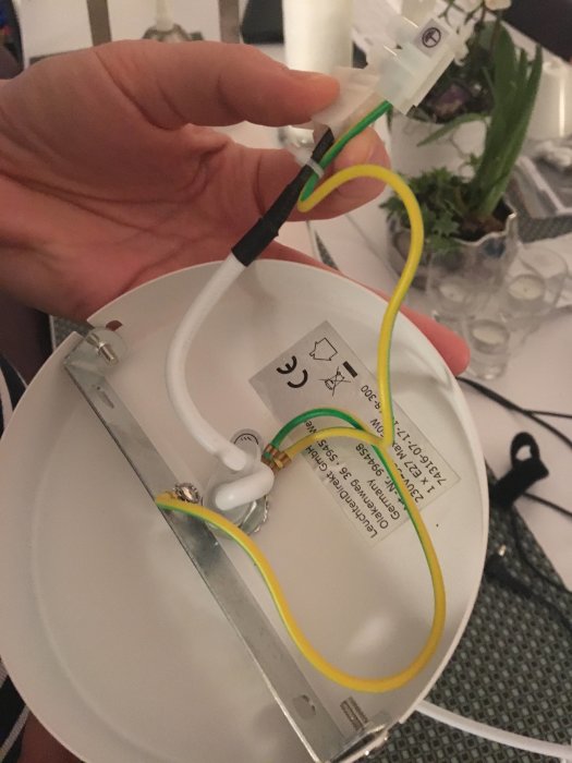 Hand håller en taklampas kabel med ojordad anslutning och metallkupa som visas uppifrån.
