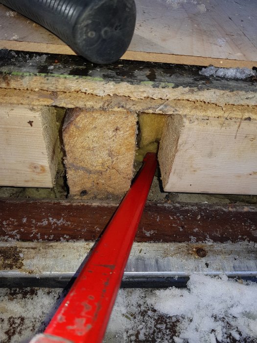 Sågat hål i trägolv som avslöjar en underliggande betongplatta, med kofot och snörester.