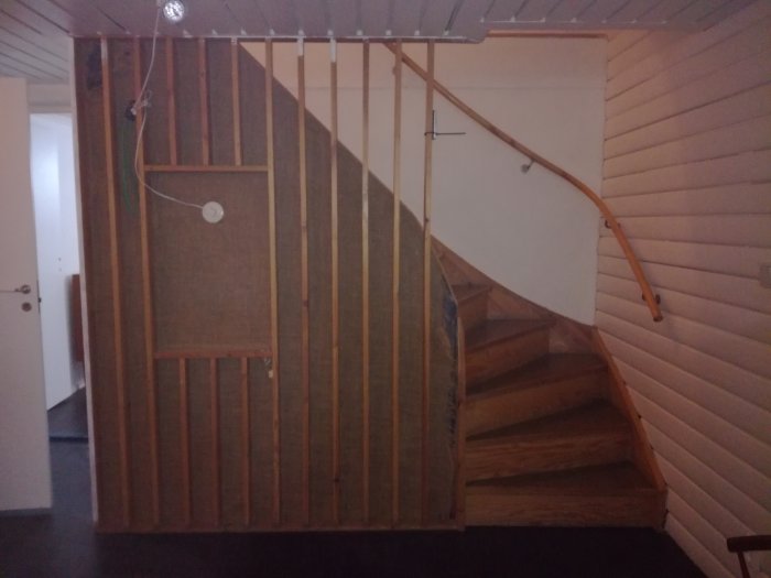 Äldre trapp med träreglar spikade över trasig väv vid en spaljé med en fyrkantig ram och ett insläpp av ljus ovanför.