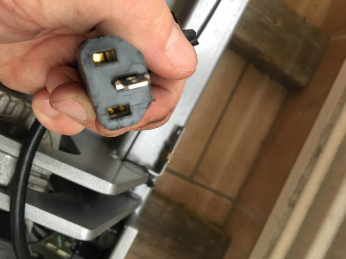 Hand håller en skadad C13-liknande apparatkabel med brytare och extra stift.