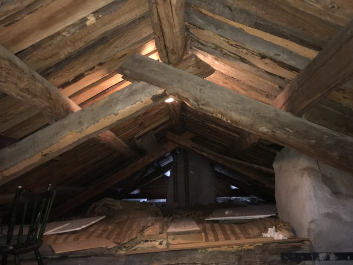 Gamla träbjälkar och stockar synliga i en oisolerad vindstruktur med spånläkt på ett hus från 1860.
