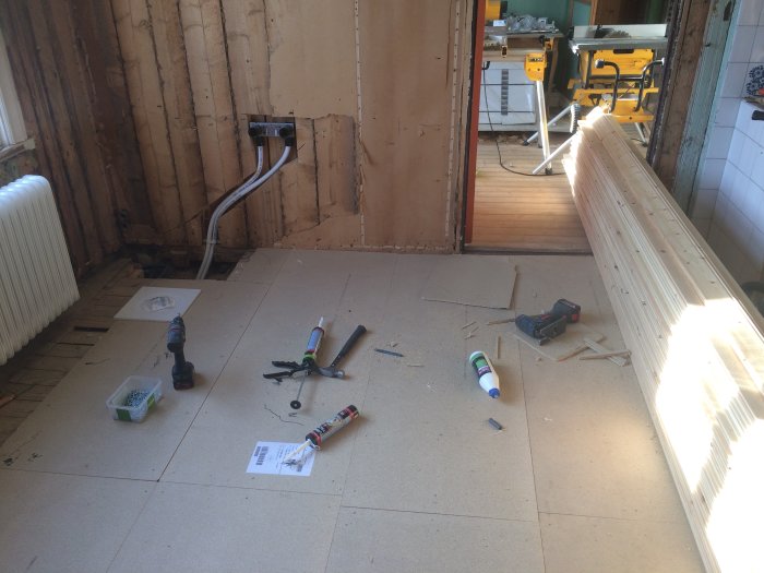 Renoveringsprocess i badrum med isolering och nytt golvspån, verktyg och byggmaterial utspridda.