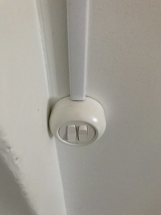 Vit vägggenomföring för kabel med två knappar på en sockel.