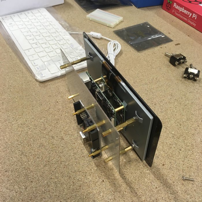 Raspberry Pi-skärm med elektroniska komponenter monterade på genomskinlig akrylplatta på ett arbetsbord med verktyg.