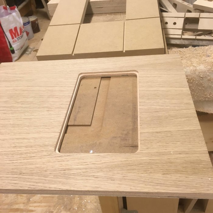Björkplywood med fräst monteringsöppning för elektronikprojekt, arbetsbänk i bakgrunden.