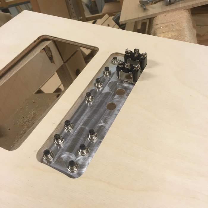 Hörn av ett träbord med en elektronisk komponent monterad på en aluminiumplatta som har borrade hål och sitter på träyta.
