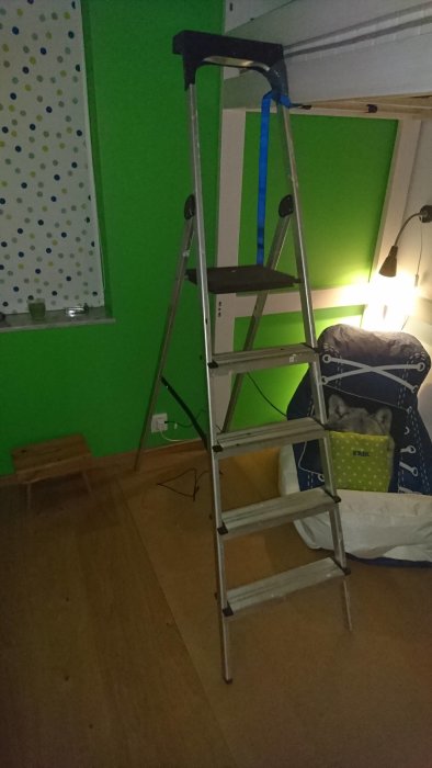 Stege med blå spännrem fastsatt vid en provisorisk hylla i ett rum med grön vägg och masonitskiva på golvet.
