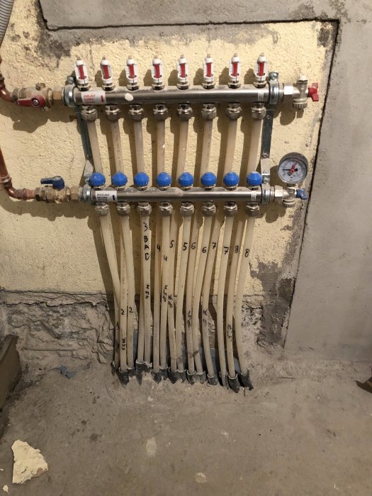 Golvvärmerör och fördelare som kommer upp ur betongplatta, omslutna av betong och isolering.