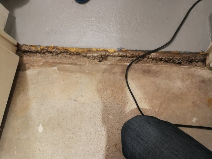 Skadad källarvägg och golvkant med avflagning och kabel över ytan.