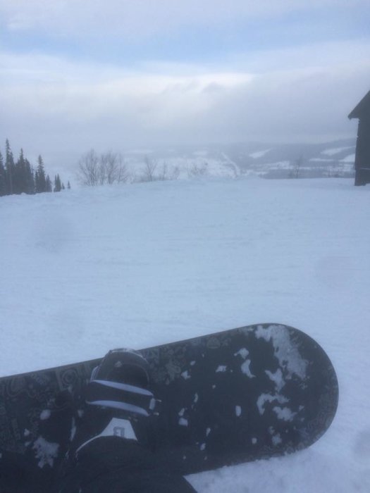 Snowboard på snötäckt sluttning med dimmig utsikt över ett vinterlandskap.