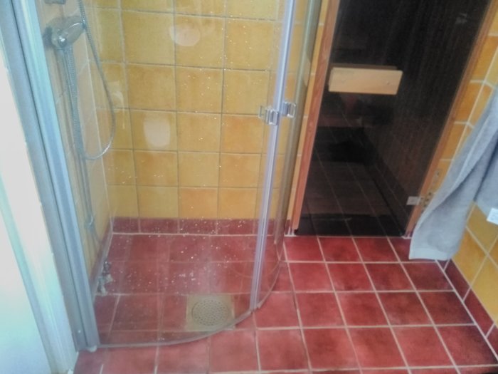Hörndusch med buktande glasväggar, gul kakelvägg och rött kakelgolv som leder till en bastu.