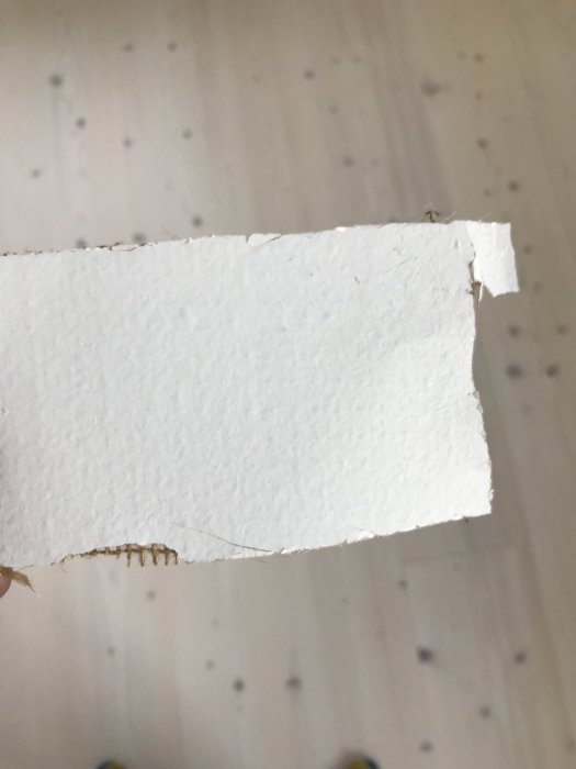 Hand håller bit vit takpapp eller takväv med trasig kant mot suddig bakgrund.
