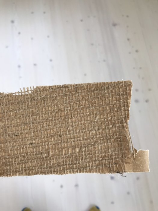 Bit av brunt, vävt material som liknar takpapp eller takväv hålls upp mot vit bakgrund.