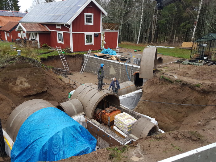 Byggarbetsplats för vinkällare med halverade betongrör, isoleringsmaterial och arbetare.