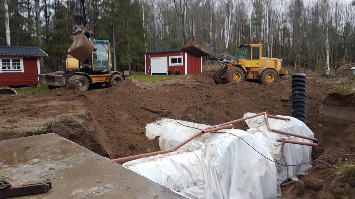 Byggarbetsplats för vinkällare med grävmaskiner, högar av jord och synliga markisoleringsrör.