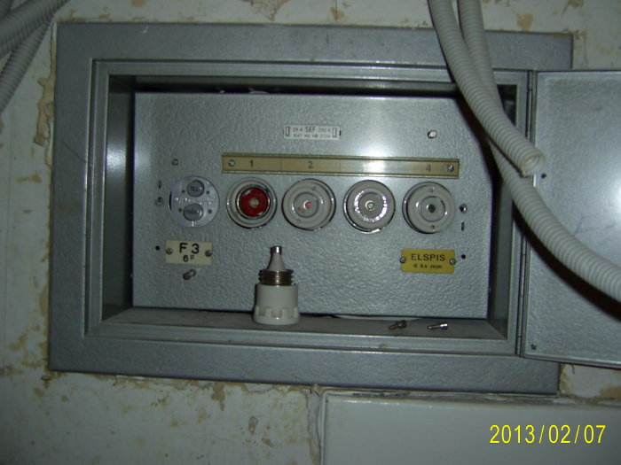 Gammal elcentral med flera vred och en etikett märkt "ELSIPS", omgiven av slitage och äldre ledningsrör.