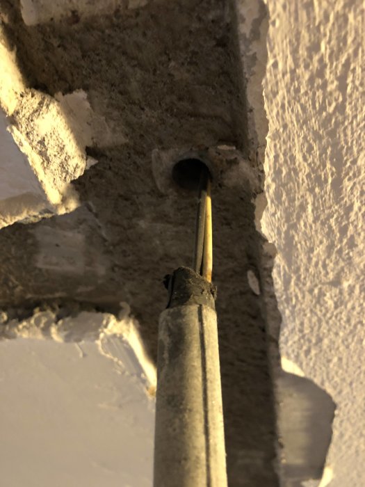 Aluminiumskyddsrör med kablar går genom en öppning i en betongvägg under renovering.
