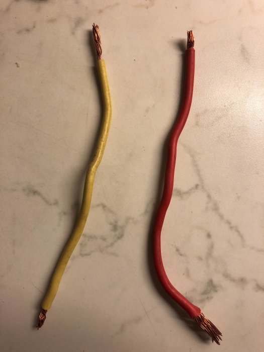 Elektriska kablar med avskalade ändar i gult och rött ligger på en marmoryta.