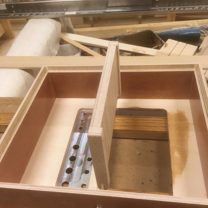 Träkonstruktion av elektroniklåda med falsade hörn och vridbar metallplatta i verkstadsmiljö.