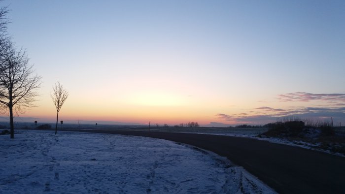 Solnedgång med snötäckt mark och träd silhuetter mot en färgrik himmel.