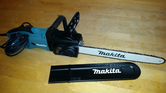 Makita elektrisk motorsåg med 16-tums svärd, ligger på trägolv med strömkabel och skydd.