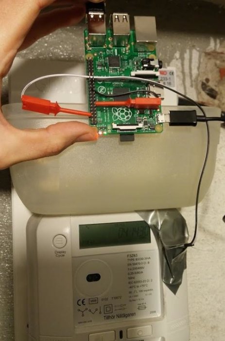 En hand håller en Raspberry Pi-kortdator ansluten till en fotoresistor över en elmätare med en ljusdiod.