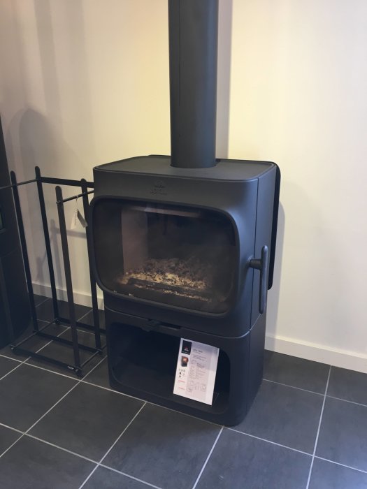 En nyinstallerad Jøtul F305 kamin med korta ben på grå klinkergolv, skyddad av en svart grind, klar för användning i ett hem.