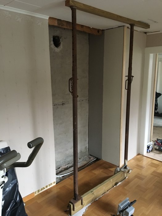 Renoveringsarbete med stöttor i vardagsrum för att installera kamin, med skorsten och avtäckt golv.