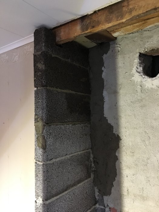 Renoveringsarbete med uppstöttad takbjälke och delvis putsad murvägg förberedd för kamininstallation.