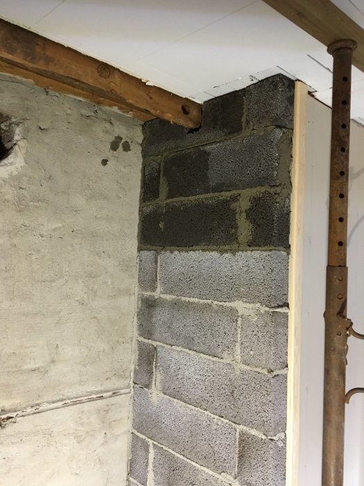 Delvis renoverat hörn av ett rum med synliga gråa murblock och stöttor under förberedelser för kamininstallation.